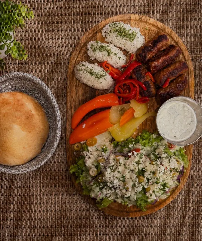 Planche de qebap avec riz, poivrons, salade au fromage, sauce au yaourt et pain maison
